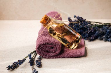 Menekşe havlusuna yakın plan lavanta yağı ve bej renkli taştan arka planda lavanta çiçekleri. Ön görünüm