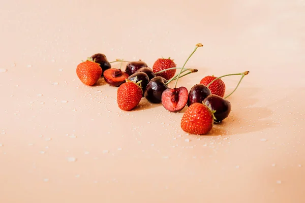 Big ripe cherry and strawberry with water drops on light orange background in sunlight. Front view