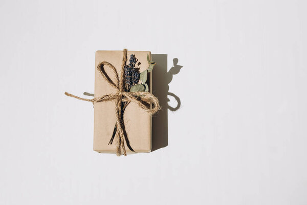 The gift is wrapped in kraft paper and tied with twine with dry lavender and eucalyptus on a white background. Top view