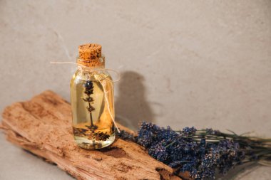 Lavanta yağı, lavanta çiçekleri olan hafif taştan bir arka planda, ahşap bir tezgahta. Ön görünüm