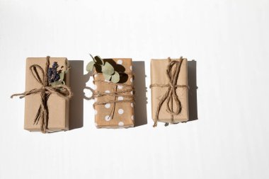 A set of handmade gifts in kraft paper, tied with wide twine, decorated with dry flowers on a white table. Top view