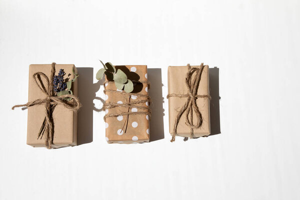 A set of handmade gifts in kraft paper, tied with wide twine, decorated with dry flowers on a white table. Top view