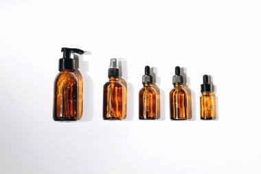 Five clear amber bottles with natural cosmetics on a white background. Top view
