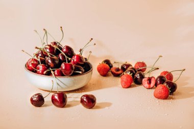 A large cherry with water drops close up in a gray deep plate on a light orange background in sunlight, selective focus. Front view