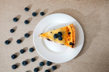 A piece of blueberry cheesecake on a white plate on a stone background. Top view
