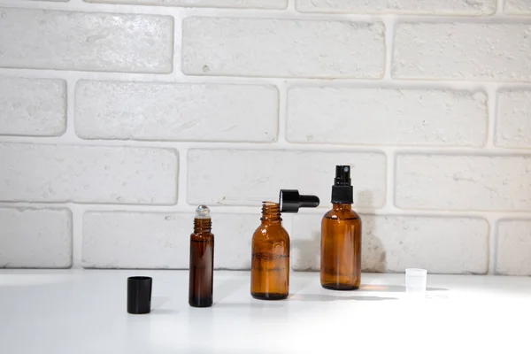 Tree open amber bottles with natural cosmetics on a white table and brick wall. Front view
