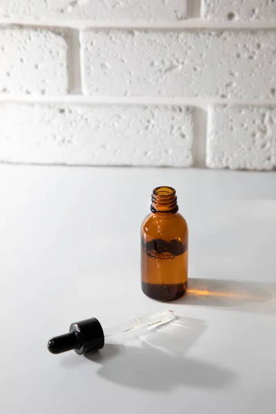 One open amber bottle with a pipette on a white table, selfcare cosmetic products. Front view