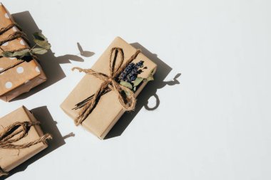 A set of handmade gifts in kraft paper, tied with wide twine, decorated with dry flowers on a white table. Top view