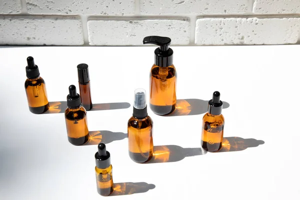 A group of amber bottles on a white table with face care products. A set of cosmetics in a glass package. Front view
