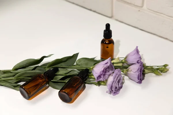 A group of amber bottles on a white table with face serum products near purple eustoma. Glass bottle with self care product. Top view