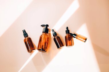 A group of amber bottles on an orange table with face care products. A set of cosmetics in a glass package. Top view