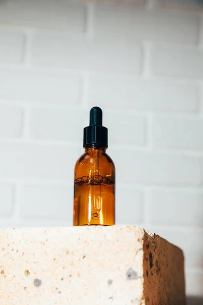 An amber bottle on a brick with face serum product. Glass bottle with self care product. Front view