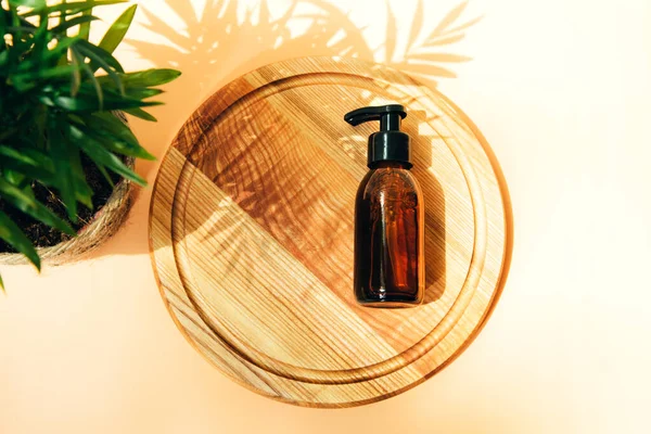 Face cleanser in amber bottle on a wooden board and green plant. Glass bottle with self care product. Top view