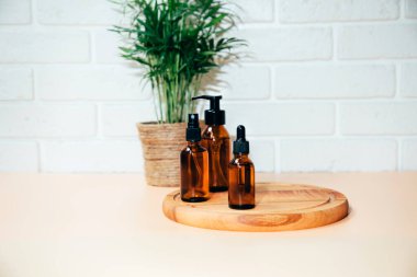 A group of amber bottles on wooden board with face care products. A set of cosmetics in a glass package with a house palm in the background. Front view