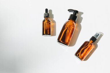 A group of amber bottles on an white table with face care products. A set of cosmetics in a glass package. Top view