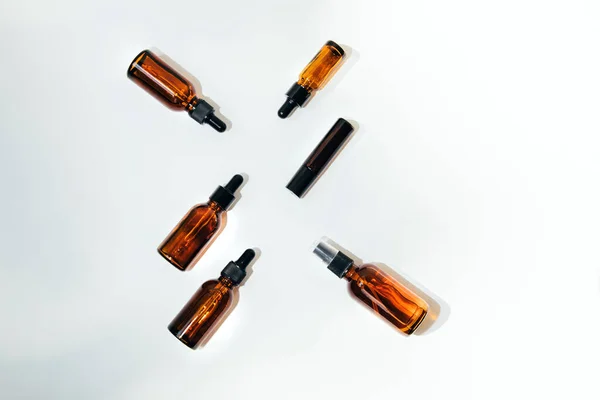 A group of amber bottles on an white table with face care products. A set of cosmetics in a glass package. Top view