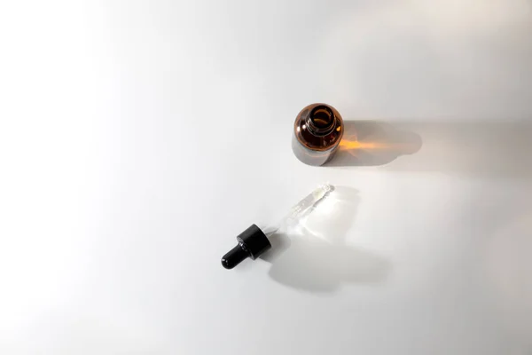 One amber open bottle with pipette on an white table with face care product. Top view