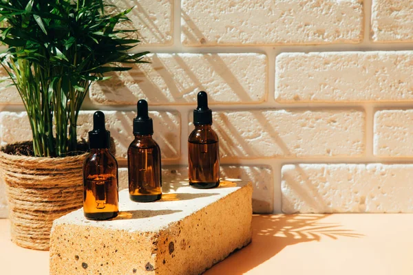 A group of amber bottles on brown brick with face care products. Serum in a glass package with green palm on background. Front view