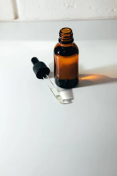 One amber open bottle with pipette on an white table with face care product. Top view