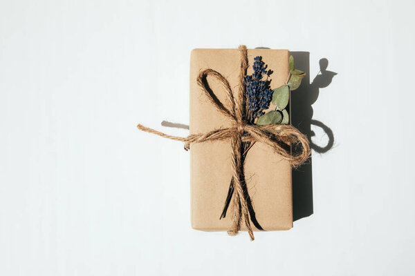 The gift is wrapped in kraft paper and tied with twine with dry lavender and eucalyptus on a white background. Top view