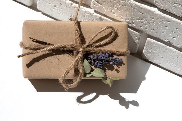 The gift is wrapped in kraft paper and tied with twine with dry lavender and eucalyptus on a white background. Top view