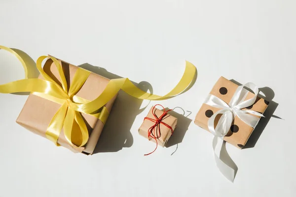 A set of gifts wrapped in kraft paper with yellow, blue, white and red ribbon with shadow on a white background. Top view