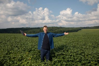 A farmer with a tablet checks the quality of soybeans in an agricultural field and is happy with the harvest. Front view