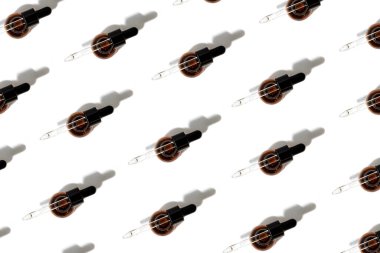 Pattern of open amber bottle with pipette on an white table with face care product. Top view