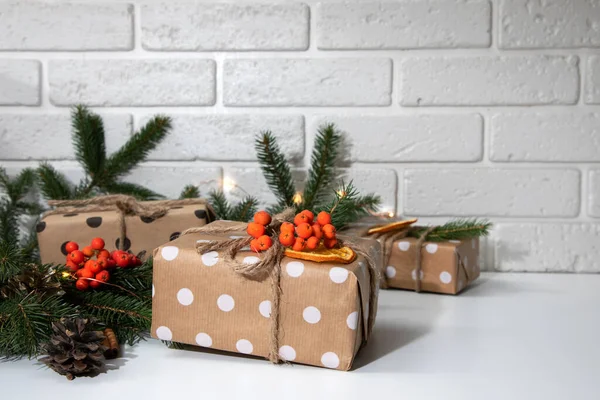 一组礼物在生态包装 用褐色纸包着白色圆圈 装饰着干橙 山灰和冷杉枝条 新年礼物 白色桌子上的灯 前景色 — 图库照片