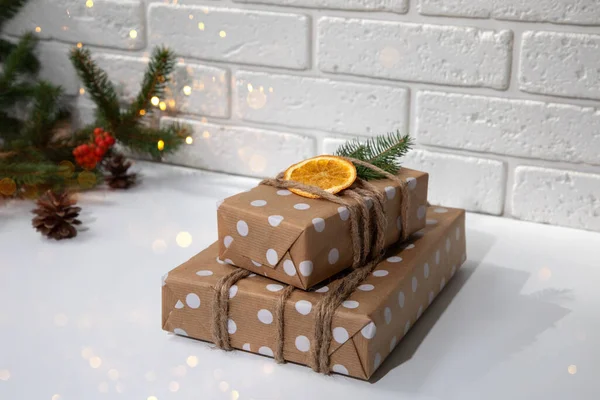 生态包装中的两件礼物 用褐色纸包着白圈 装饰着干橙和冷杉枝条 新年礼物 白色桌子上的灯 前景色 — 图库照片