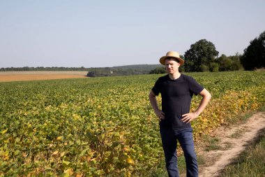 Hasır şapkalı ve koyu mavi elbiseli bir çiftçi soya fasulyesiyle tarla tarlasına bakıyor. Ön görünüm