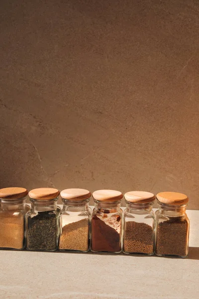 A group of seasonings in glass jars on a light stone background with shadows. Paprika, herbs, mustard, garlic, front view, selective focus