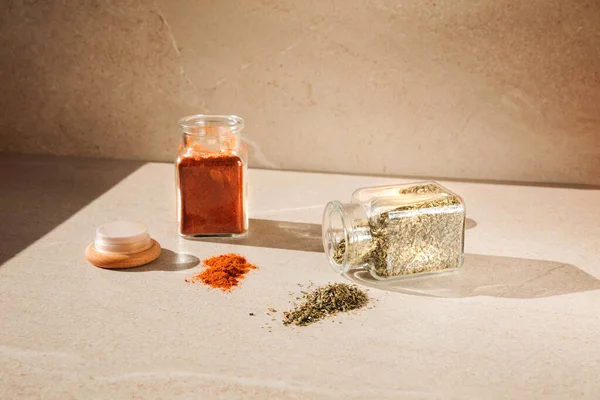 Seasonings in glass jars on a light stone background with shadows. Paprika and dry herbs in open bottles front view, selective focus