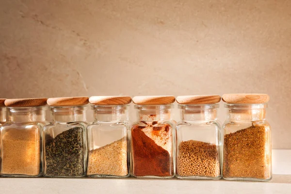 A group of seasonings in glass jars on a light stone background with shadows. Paprika, herbs, mustard, garlic, front view, selective focus