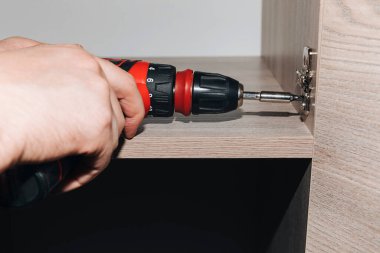 Bir dolabı monte ederken kırmızı bir tornavidayla erkek ellerine yakın çekim. Ön görünüm, seçici odak