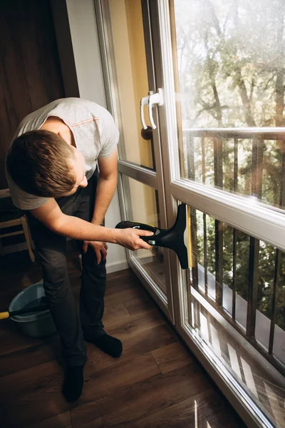 A man washes windows at home using a cordless window vacuum cleaner. Front view, selective focus