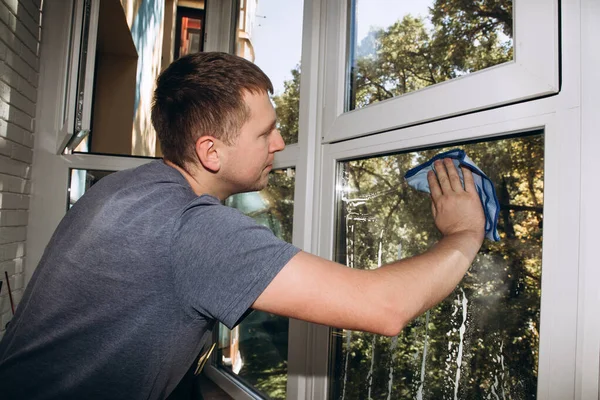 A man washes windows at home using a blue rag, cleaning the house close-up. Front view, selective focus