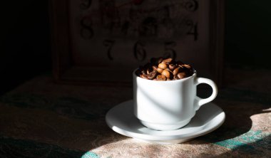 Koyu arkaplanda beyaz seramik fincanda kahve çekirdekleri.