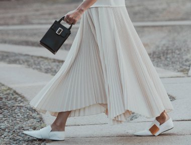 Milan, İtalya - 24 Eylül 2021: sokak tarzı kıyafet, krem rengi beyaz polo giyen şık kadın, pileli etek, Milano sokaklarında siyah çanta, ayrıntı.