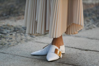 Milan, İtalya - 24 Eylül 2021: sokak tarzı kıyafet, krem rengi beyaz polo giyen şık kadın, pileli etek, Milano sokaklarında siyah çanta, ayrıntı.