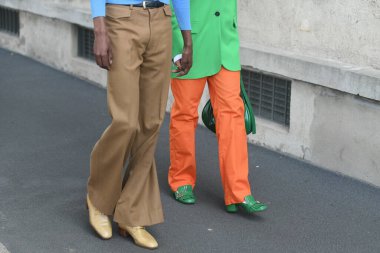 Milan, İtalya - 24 Eylül 2021: Sokak tarzı kıyafet, turuncu ve kahverengi pantolon giyen şık çift, Milano, İtalya sokaklarında yeşil ve sarı ayakkabılar.