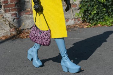 Milan, İtalya - 24 Eylül 2021: Sokak tarzı kıyafet, şık bir kadın büyük sarı bir ceket giyiyor, Prada 'dan siyah ve pembe desenli bir çanta, İtalya' nın Milano şehrinden mavi parlak deri çizmeler..