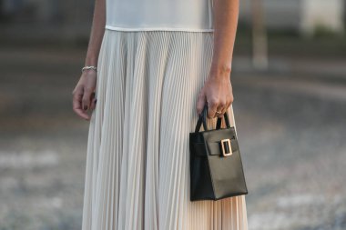 Milan, İtalya - 24 Eylül 2021: sokak tarzı kıyafet, krem rengi beyaz polo giyen şık kadın, pileli etek, Milano sokaklarında siyah çanta, ayrıntı.