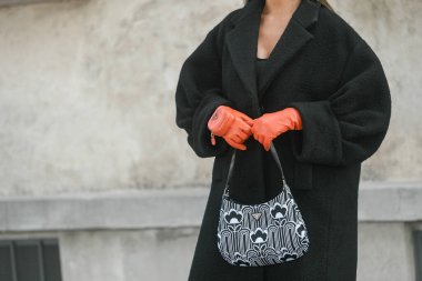 Milan, İtalya - 24 Eylül 2021: Sokak tarzı kıyafet, siyah ceket, beyaz çizme, turuncu Prada eldiven ve İtalya 'da Prada çanta giyen şık kadın.