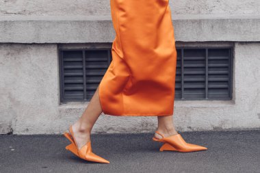 MILAN, ITALY - FEBRUARY 24, 2022: Elegant woman wearing orange long dress, black bag and white gloves.