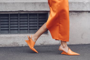 MILAN, ITALY - FEBRUARY 24, 2022: Elegant woman wearing orange long dress, black bag and white gloves.