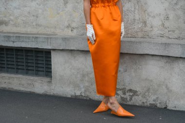 MILAN, ITALY - FEBRUARY 24, 2022: Elegant woman wearing orange long dress, black bag and white gloves.