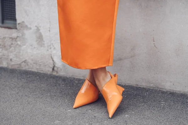 MILAN, ITALY - FEBRUARY 24, 2022: Elegant woman wearing orange long dress, black bag and white gloves.