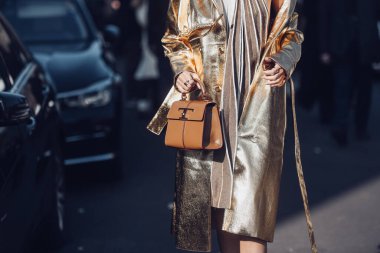 Milan, Italy - February, 25: Street style, woman wearing a beige and brown accordion halter-neck short dress, a brown shiny leather handbag, white varnished leather platform sole high heels shoes. clipart