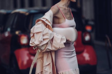 Sokak stili, soluk pembe kolsuz bluz dizli, işlemeli, soluk pembe bir midi elbise giyen bir kadın, soluk pembe, büyük boy, uzun bir trençkot ve pembe kayışlı sandaletler..